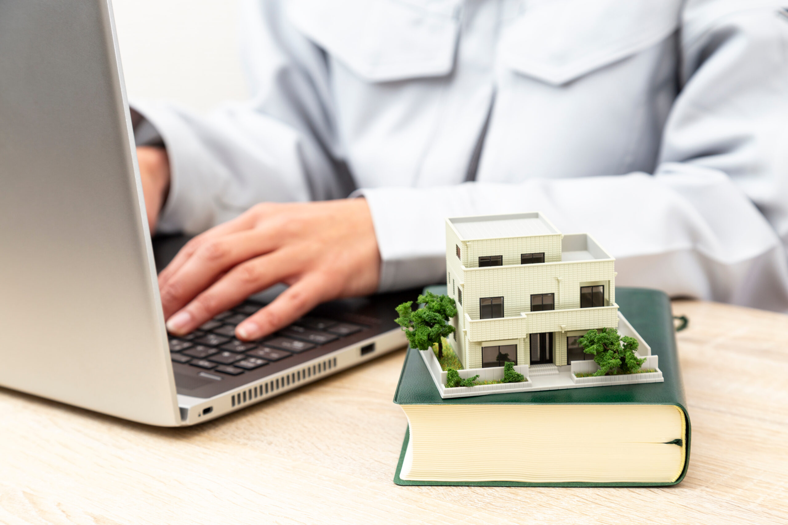 辞書の上に住宅模型を置き、パソコンで調べ物をする人物のイメージ写真。