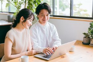 家でノートパソコンを見ながら話す夫婦
