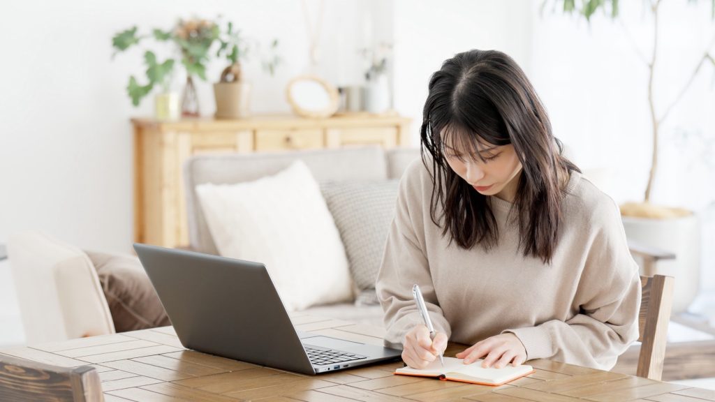 パソコンで調べ物をしメモを取る女性
